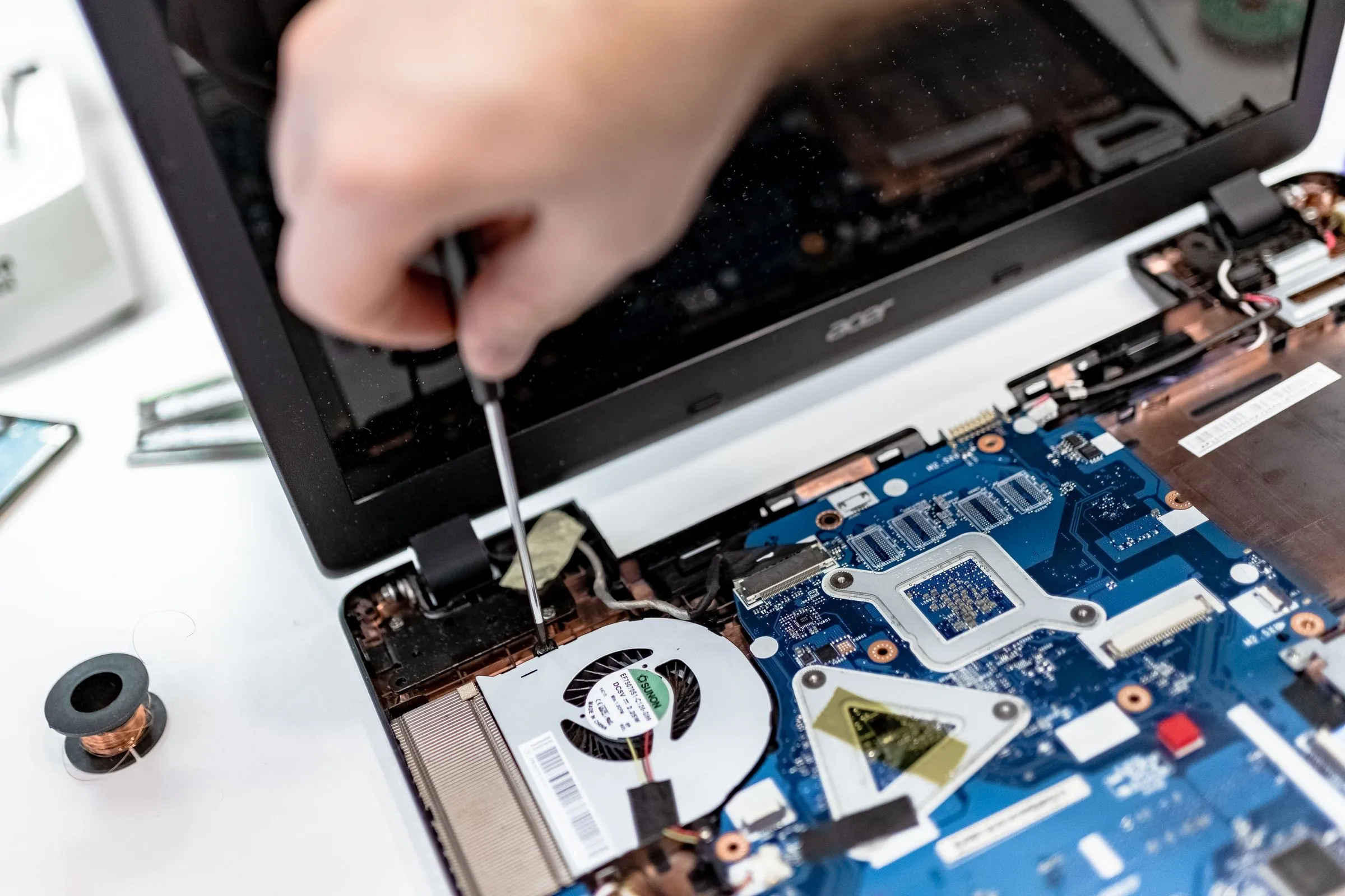 A technician repairing a laptop motherboard with a screwdriver